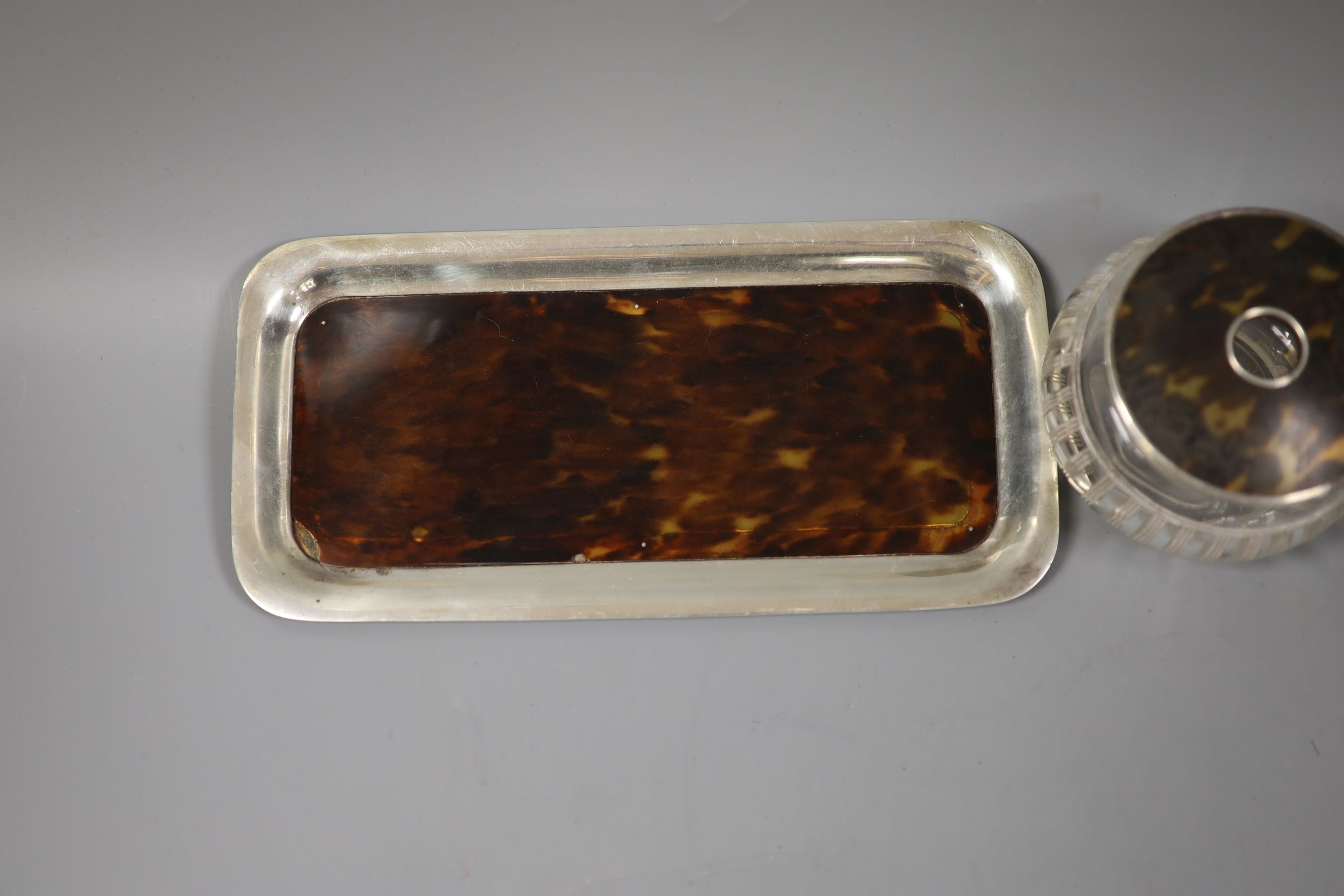 An Edwardian silver mounted tortoiseshell dressing table tray and a similar mounted glass tidy.